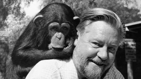 Durrell Wildlife Conservation Trust A black and white image of Gerald Durrell with a monkey on his back. He has short hair and a beard.