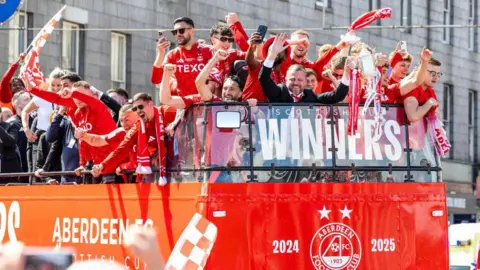 SNS A red bus with football players on top holding a trophy