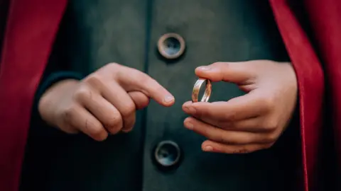 Getty Images A pair of hands belonging to a person with a green waistcoat and red cloak holding a gold ring