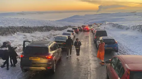 Derbyshire County Council Rows of cars on both sides of a road high up in a snowy Peak District