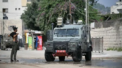 Getty Images A Palestinian youth lifts his t-shirt up to show Israeli troops that he is unarmed during a military operation in Jenin in the north of the occupied West Bank on August 29, 2024