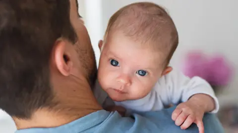 A man with his face away from the camera holding a baby looking across his shoulder