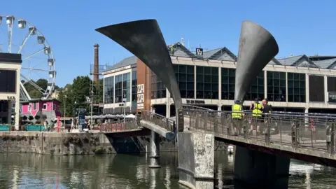 Pero's Bridge in Bristol Harbour, with workmen standing on it. One side is visibly lower than the other and off to the side. 