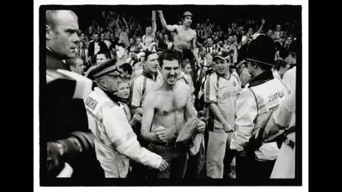 Marcus Davies Black and white photograph from 2004 of police officers controlling Torquay United fans as they celebrate beating Southend 2-1 to win promotion to the old Second Division. 
