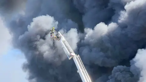 John Fairhall/BBC A firefighter using an aerial ladder to tackle the fire from above