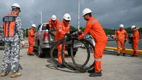 Getty Images Coast guard personnel carry a suction hose for deployment at a port in the Philippines.