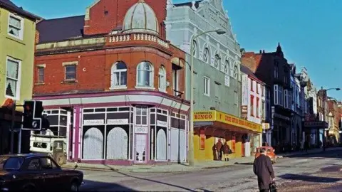 Theatre Royal Wakefield A historical picture of Wakefield, when the city's theatre was a bingo hall. The colour image shows a clear day with pedestrians walking past the building. 
