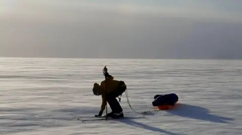 Sebastian Gjolstead Frederick Fennessy on skis pulling a sled across snow - there is only snow and blue sky visible in the background.