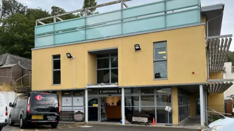 BBC The entrance of the JSPCA Animal Shelter building. It has glass-fronted wall and automatic glass doors with a yellow first floor. 