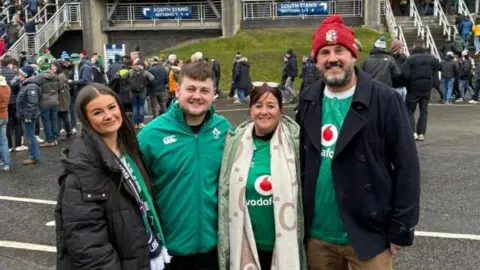 Charlie Hurst Four people in green wear Ireland rugby shirts - Áine and Charlie are smiling as are the man and woman with them. In the background are crowds and a stadium is visible