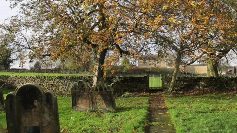 Stephen Craven/Geograph A small church graveyard with green grass and autumn trees