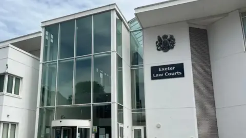 Modern white courthouse building with a large glass entrance and a sign reading “Exeter Law Courts” on the front exterior wall.