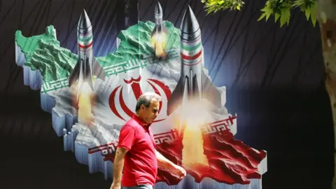 EPA An Iranian man walks past a huge anti-Israeli banner carrying pictures of missiles on Iran's map, in Tehran (19/04/24)