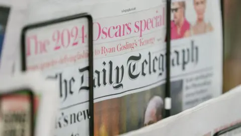 Getty Images The Daily Telegraph, showing a 2024 Oscars special, being sold connected  a paper  stand