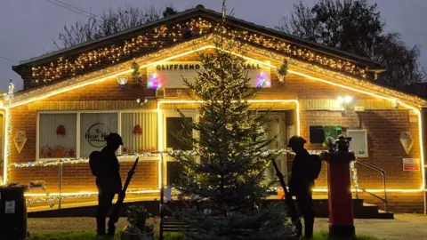 The front of a village hall is decorated with Christmas lights. 