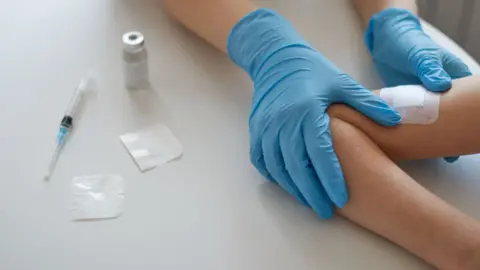 A young person's arm with a bandage after getting a jab. The jar is on the table to the left of the image