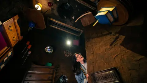 TheStoryMuseum A woman peeks in an Alice in Wonderland themed room at The Story Museum in Oxford. All the furniture is on the ceiling and it's upside down.