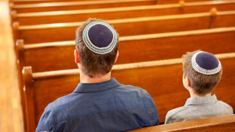 Man and boy wearing kippahs sitting on benches in a synagogue