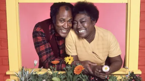 Getty Images John Amos ed Esther Rule sorridono fianco a fianco attraverso una finestra gialla in uno scatto pubblicitario per Good Times nel 1977