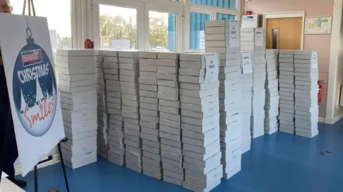 A pile of white boxes ready for delivery with a sign nearby which reads: "Little Troopers: Christmas Smiles".