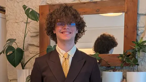 Oscar smiling at the camera. He is wearing glasses and has brown hair. 