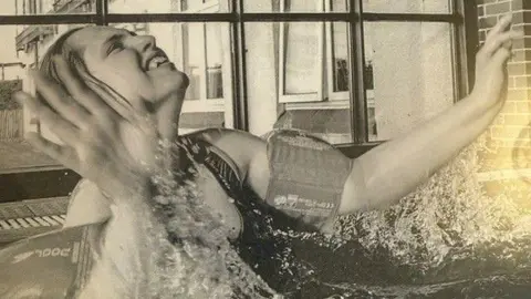 Family handout A young woman is splashing in a pool with arm bands on. She is looking up and smiling in this black and white photo.