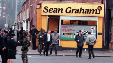 Pacemaker Press RUC officers, soldiers and people standing on the street outside the Sean Graham bookmakers.