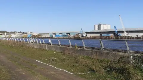 Medway Council A barren strip of land with a port in the distance across a river.