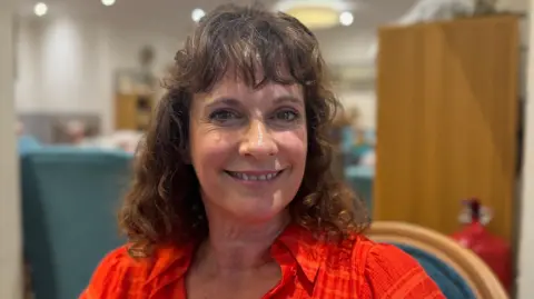 Sian Reeves with brown hair, wearing an orange shirt 