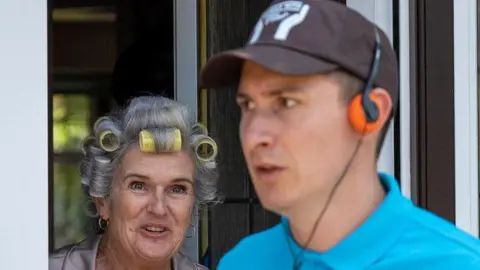 Northampton Film Festival A elderly woman with yellow curlers in her hair looks at a man in a blue polo wearing a black cap and an orange headset.