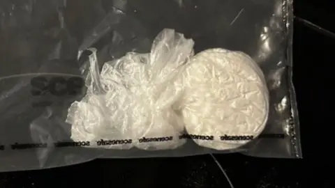 A white substance wrapped in plastic, inside a clear plastic bag on a black background. 