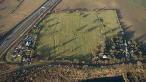 Historic England Archive Ariel view of a green field surrounded by hedges. Beneath the ground lies the remains of the Norman Cross Camp
