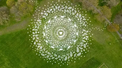Drone Studio North West An aerial shot of the artwork etched in the lush green grass of the park. It is white, 80 metres in diameter and round, with the symbols radiating out.