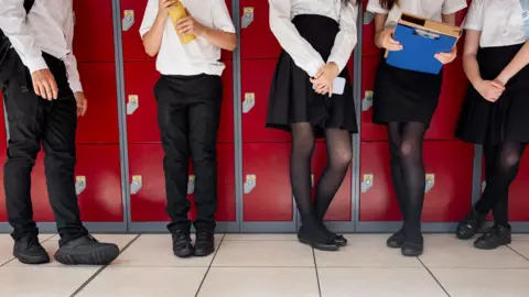 Getty Images A mixture of five female and male school students standing by some red lockers. The photo is cut off just before the pupils' shoulders.