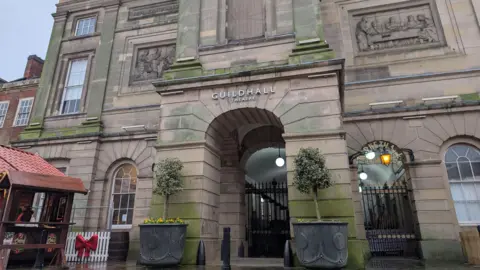 The stone entrance to the Guildhall Theatre in Derby, with black and gold gates signalling its long-term closure.