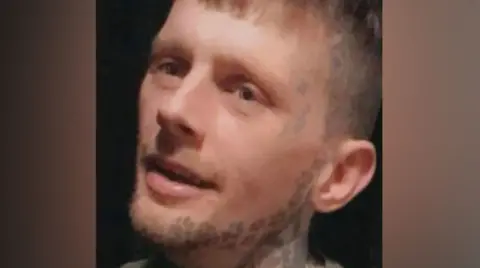 The head of a man with short light brown hair and a beard