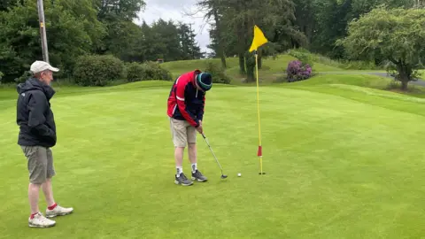 A man watches a man putt a ball