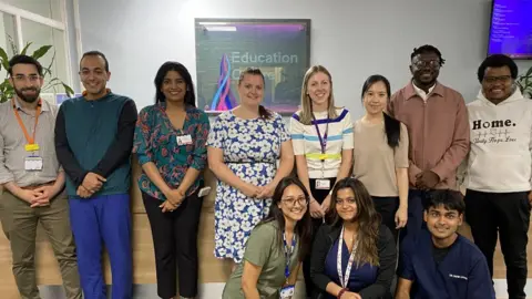 Blackpool Teaching Hospitals Eleven of the trainee doctors, dressed in casual clothing and smiling in front of a reception desk at the hospital