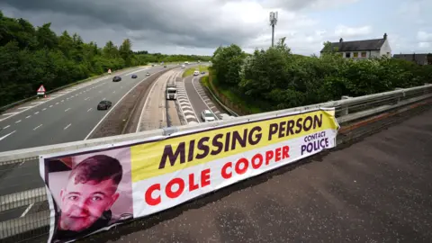 PA Media A banner featuring Cole Cooper's face and name alongside a missing person appeal asking for police to be contacted hanging over a motorway.