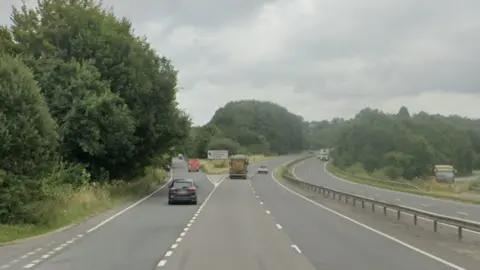 Google image of the A38 near the B3372 off slip. A car is turning off at the junction. A lorry continues along the dual carriageway. A central reservation separates the carriages.