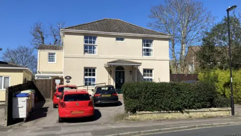 The front of a cream coloured building with three cars parked outside