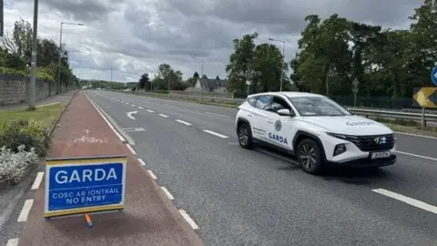 A blue garda sign and white garda car on the road