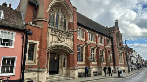 Ben Parker/BBC Ipswich County Library - a red brick, two-storey building with an ornate archway entrance made of pale stone, and an arched window above it.