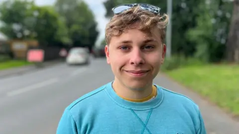 Adam Wheeler has black sunglasses on his head and is wearing a light blue sweatshirt