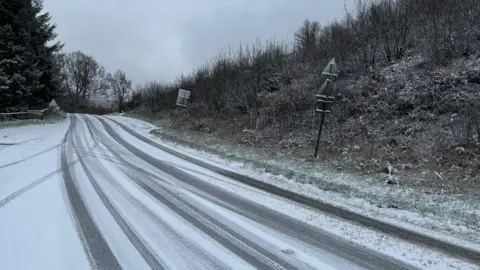 A photo taken from the bottom of a road which is covered in a thin layer of snow and has car track marks all over it. 