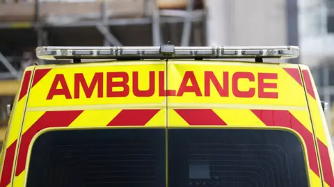 PA Media A picture of the back of an ambulance that is yellow and red in colour. There is writing that says AMBULANCE on it, with black windows below.