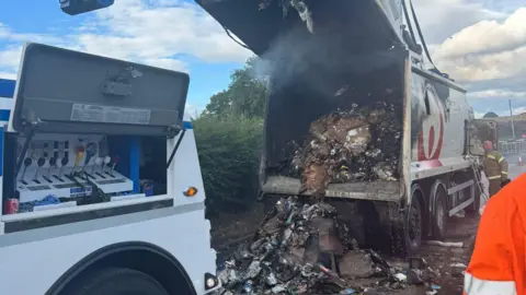 Nottinghamshire Fire and Rescue Service The rear of the bin lorry has been opened, with large amounts of burnt waste spilling out