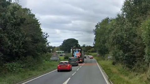 A section of the A66 at Kirkby Thore. The road is single carriage with several vehicles and a 40mph sign can be seen in the distance. There are fields and trees either side of the road.