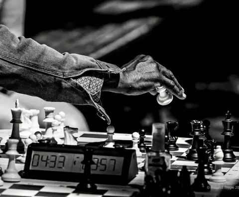 Roland Tropity is close to the hand that holds a piece of cheese over the chess panel with a temporary close