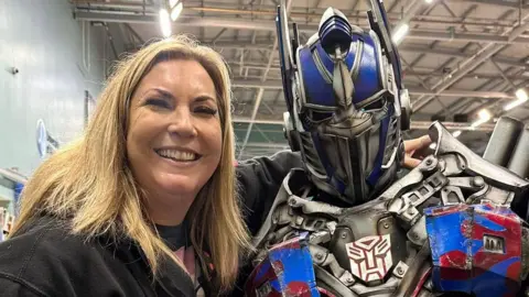 Zoe Crofts is smiling dressed in black and stood next to somebody dressed as Optimus Prime from Transformers.